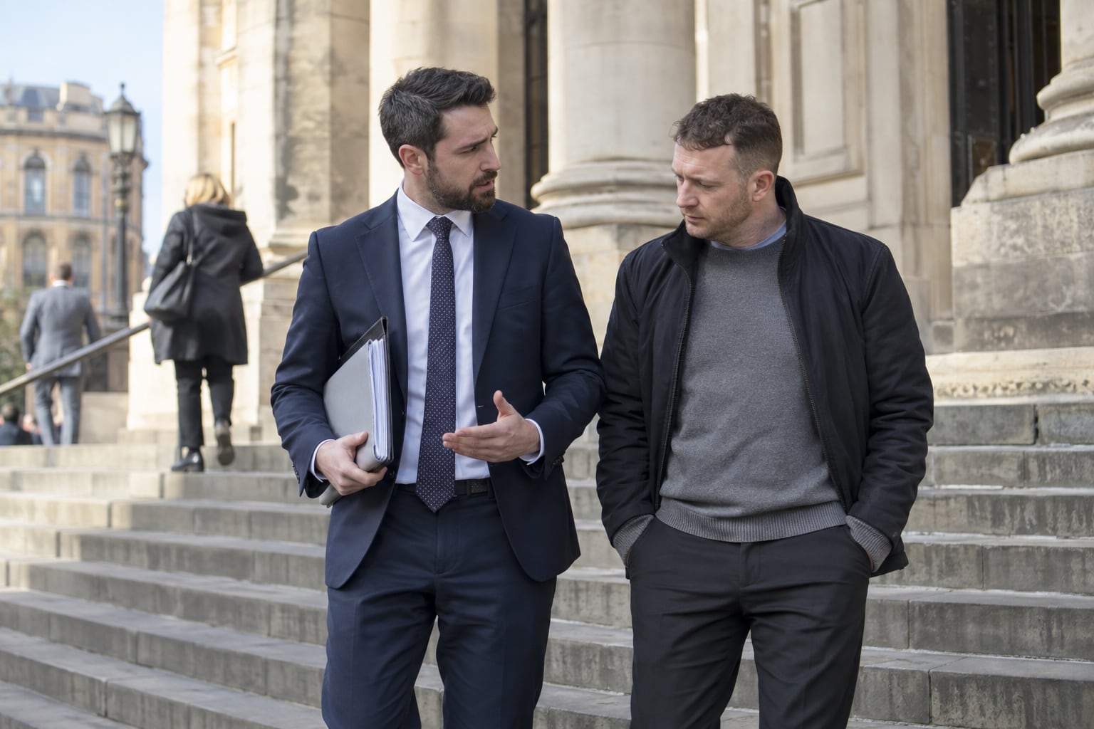 A defence solicitor speaking with a client outside a courthouse in an English city.