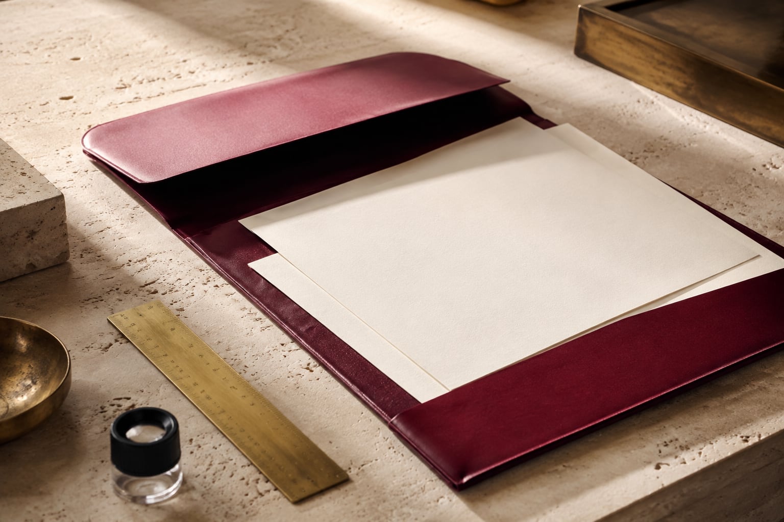 An open burgundy portfolio and optical loupe on a pale limestone review table.