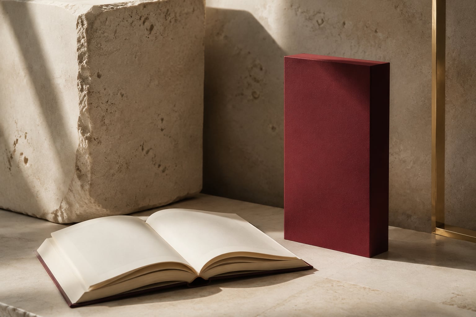An open ivory book beside a tall burgundy volume on a limestone surface.