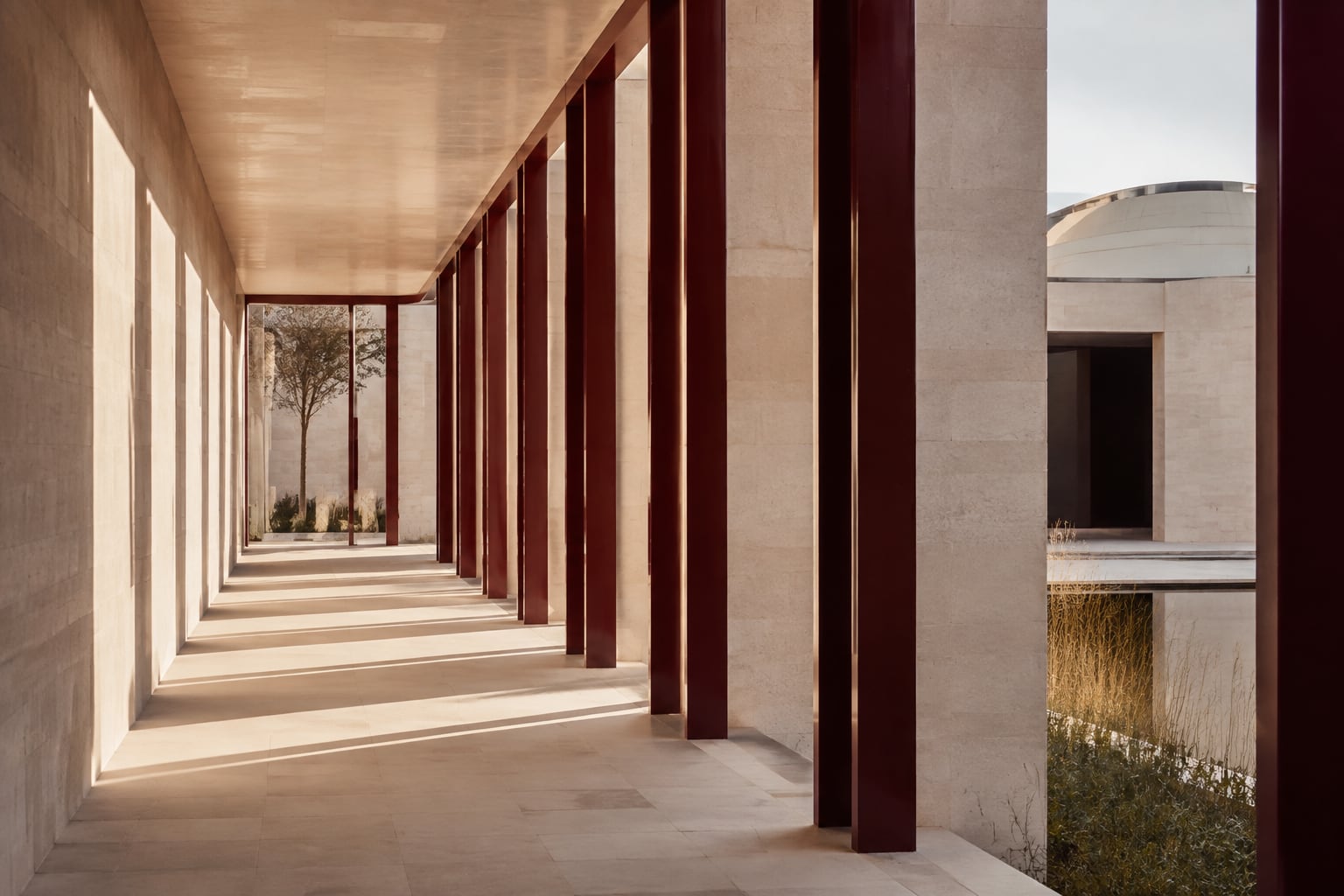 Burgundy structural frames along a light-filled limestone colonnade.