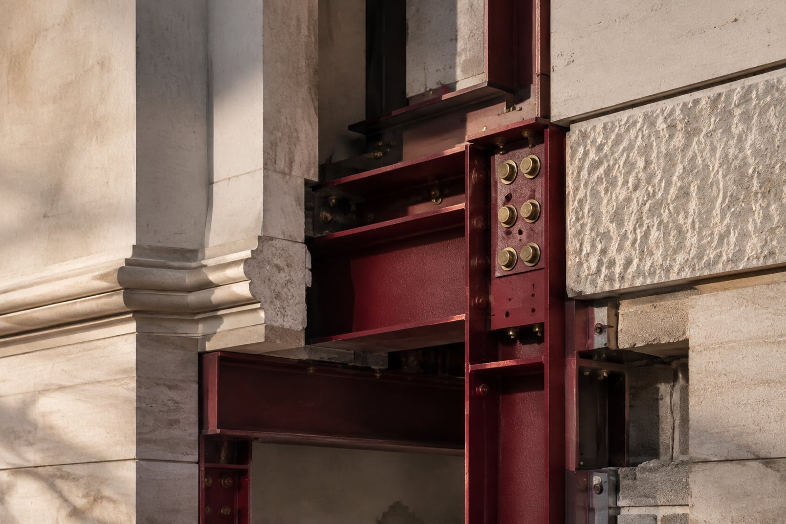 Exposed burgundy architectural framework supporting a carefully aligned limestone facade.